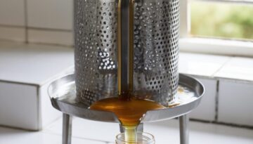 Stainless steel manual honey press machine extracting honey from crushed comb in a Kenyan beekeeping facility, showing honey dripping into collection container